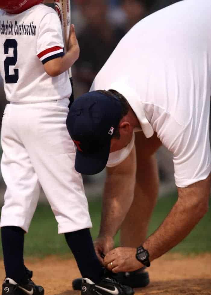 Coaching tying young athletes shoe playing baseball | What are the Responsibilities of a Youth Sports Coach?
