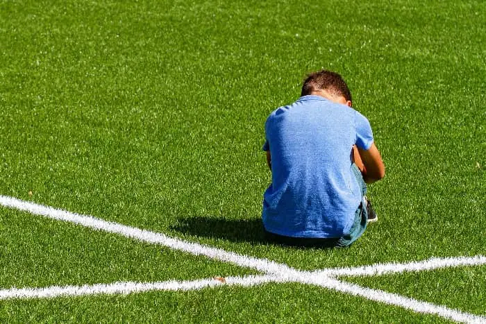 Boy sitting on sports field | What are the Challenges of Coaching Youth Sports?