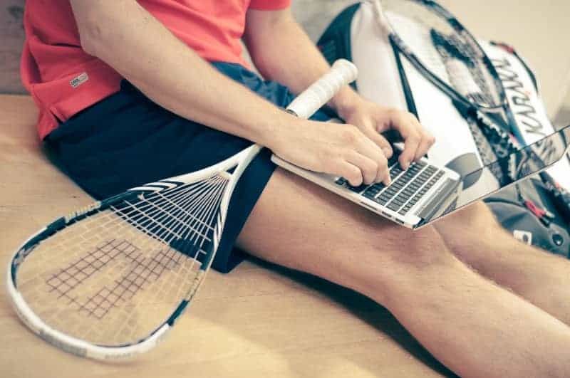 Man with tennis racket typing on laptop |Can You Coach a Sport You Never Played at the Youth Level?