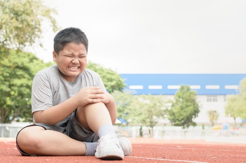 Child holding his knee in pain | How Can Poor Coaching Cause Injuries in Youth Sports?