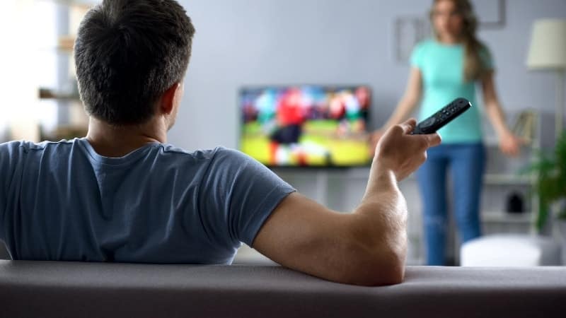 Man watching TV with women standing infront | My Husband Is a Coach and I Hate It. But Is All Hope Lost?
