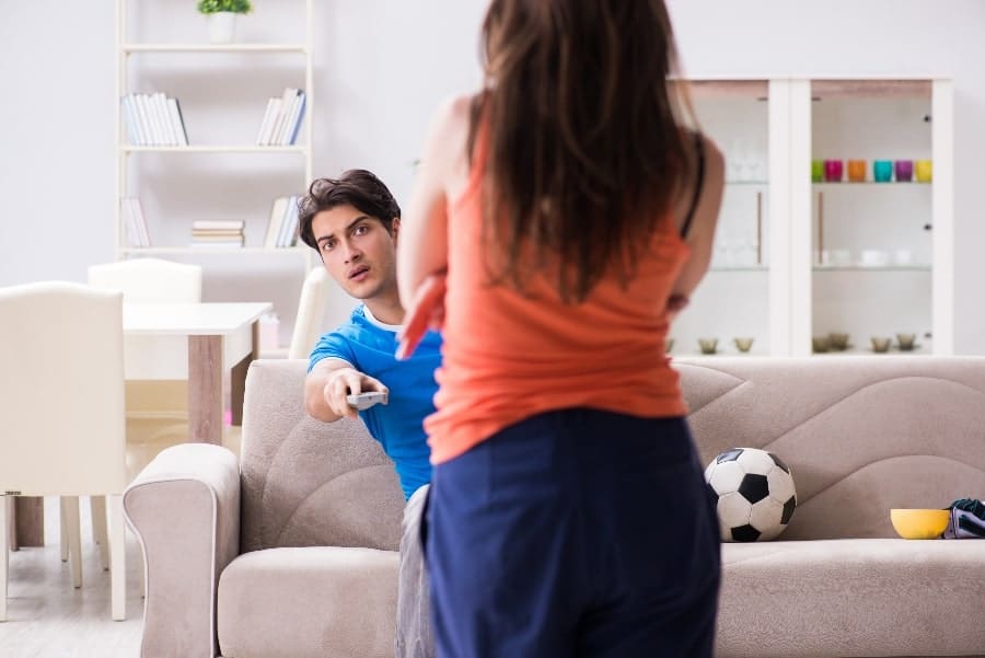 Man looking around women pointing TV remote | My Husband Is a Coach and I Hate It. But Is All Hope Lost?